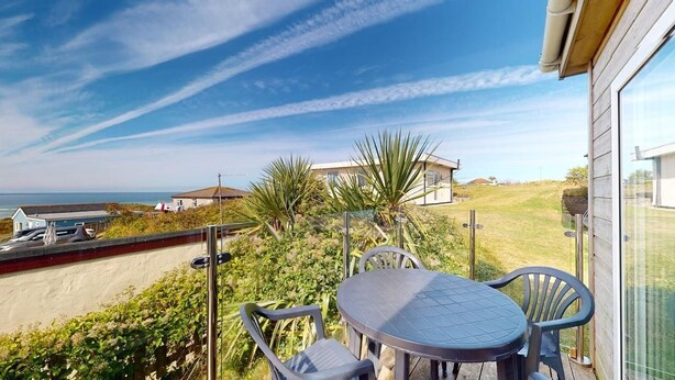 A balcony with a table and chairs, overlooking a grassy area and a building with a sloped roof. - C23 Wilmar, Riviere Towans (Hayle)