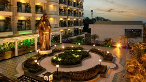 A hotel courtyard with a central statue, surrounded by landscaped gardens and illuminated by ambient lighting. - Phoenix Resort Bac Ninh (Vu Ninh)