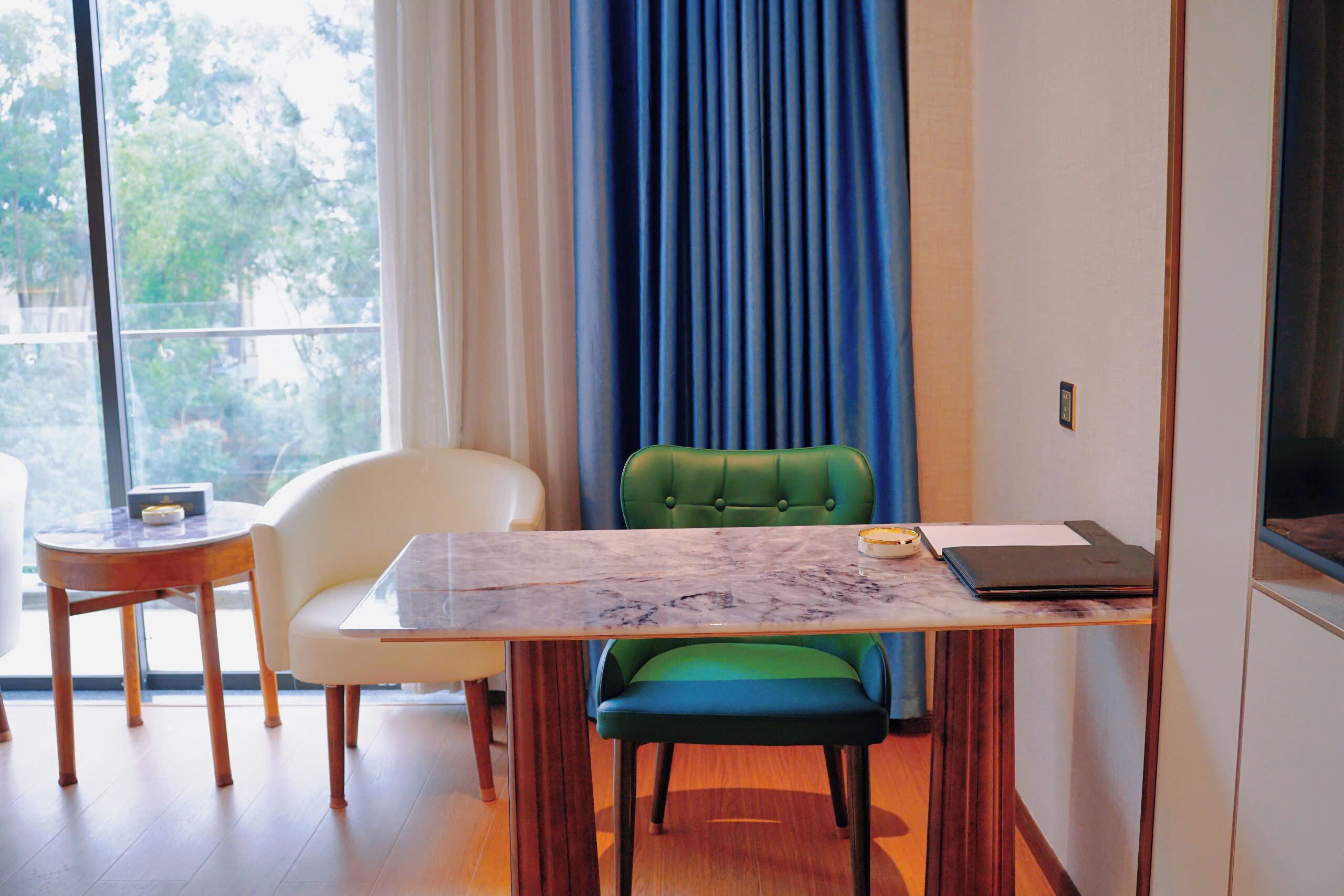 A modern room with a dining table, chairs, a laptop, and a view of greenery outside.