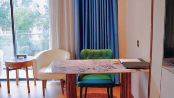 A modern room with a dining table, chairs, a laptop, and a view of greenery outside.