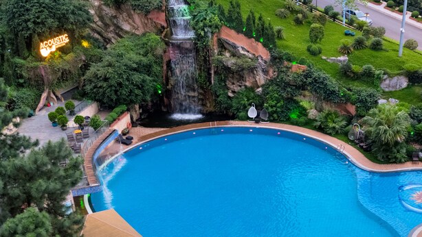 A swimming pool with a waterfall, surrounded by lush greenery and a sign that reads "ACOUSTIC." - Phoenix Resort Bac Ninh (Vu Ninh)