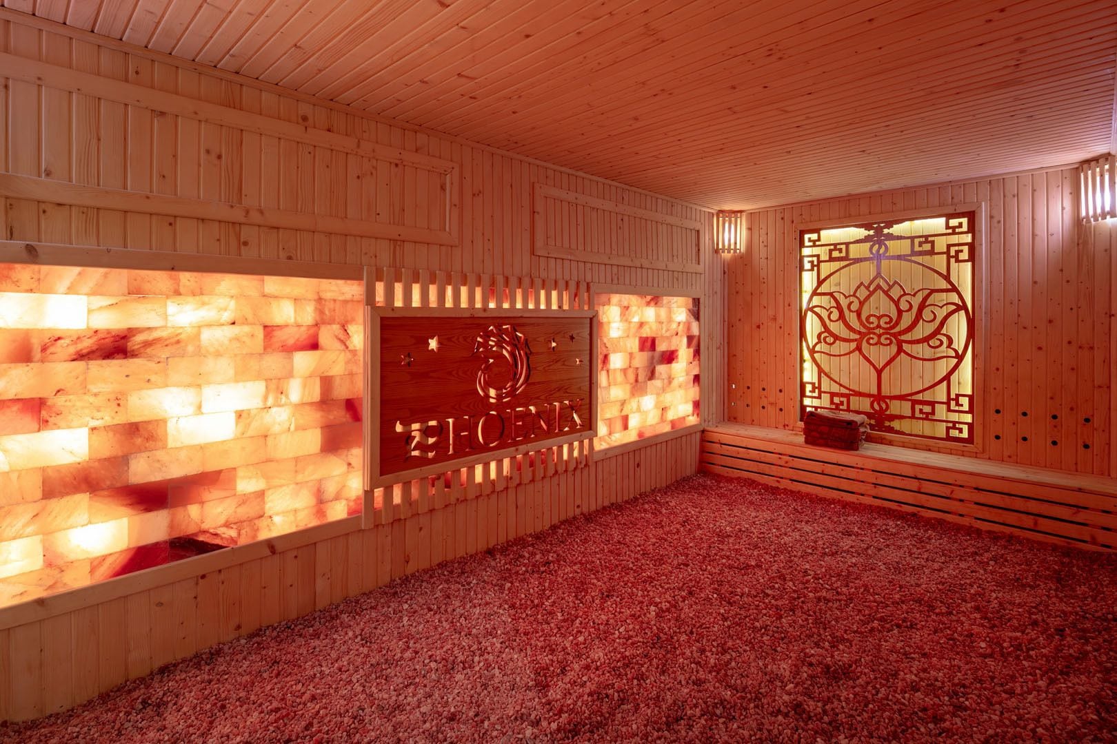 A sauna room with wooden walls, a wooden ceiling, and a floor covered with red pebbles.