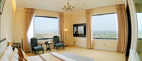 A hotel room with a large bed, two armchairs, a TV, and a view of the city.