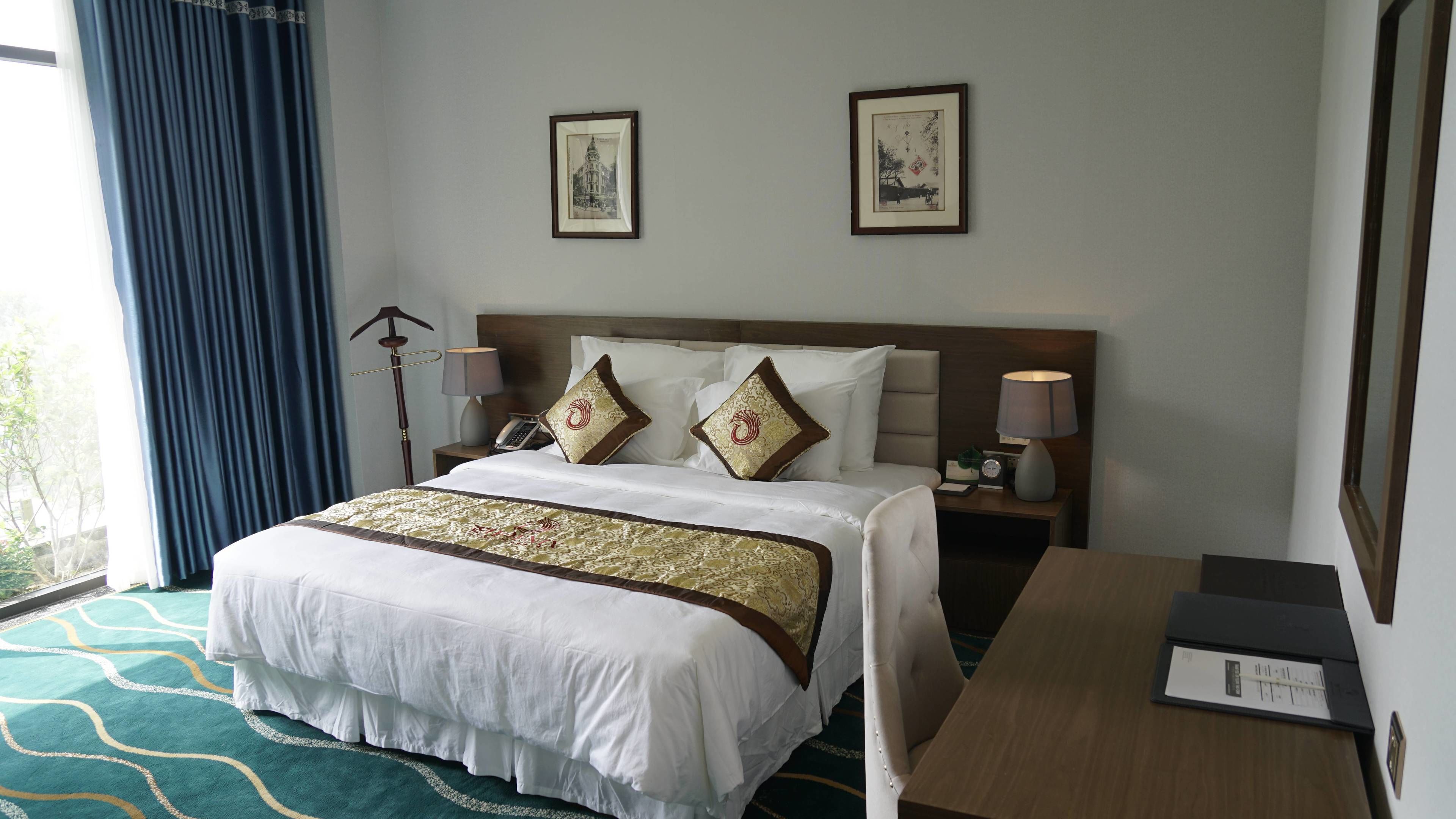 Habitación de hotel con cama, mesitas de noche, escritorio y dos cuadros en la pared.