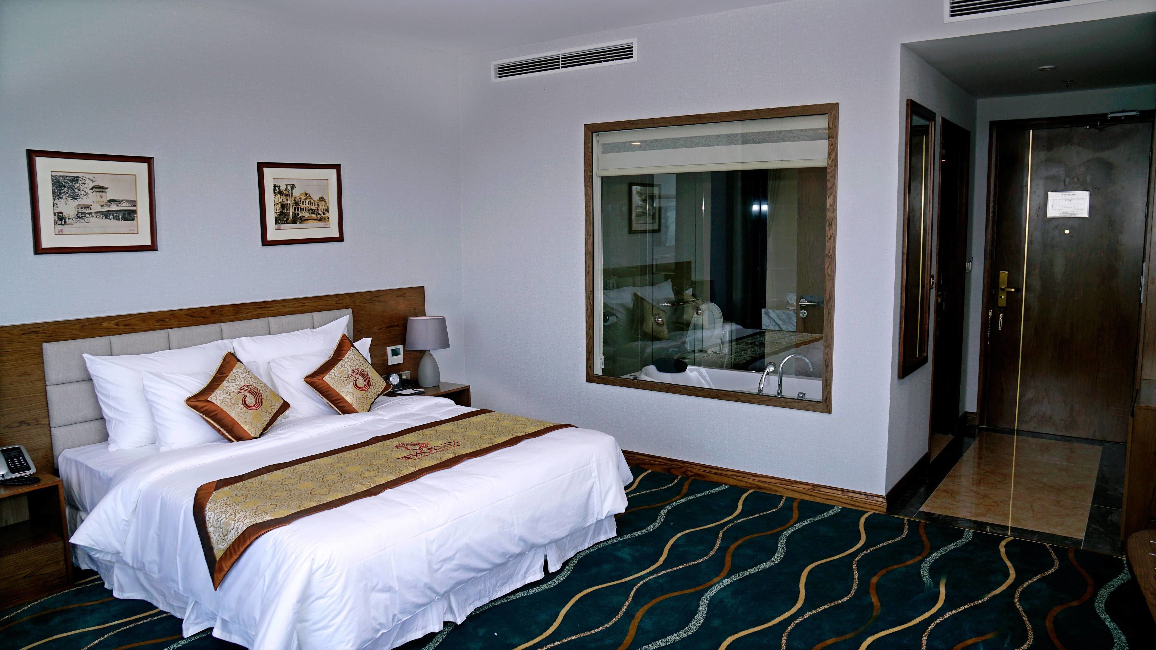 A hotel room with a large bed, a nightstand, a bedside lamp, a large mirror, and a door to the bathroom.