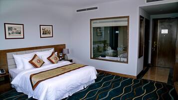 A hotel room with a large bed, a nightstand, a bedside lamp, a large mirror, and a door to the bathroom.