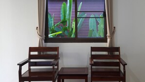 Una habitación con dos sillas de madera y una mesita, una ventana con cortinas, y vista a plantas verdes en el exterior.