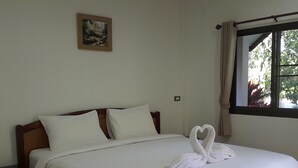 Una cama bien tendida con sábanas blancas y dos almohadas. En la cama, una toalla dispuesta en forma de corazón.