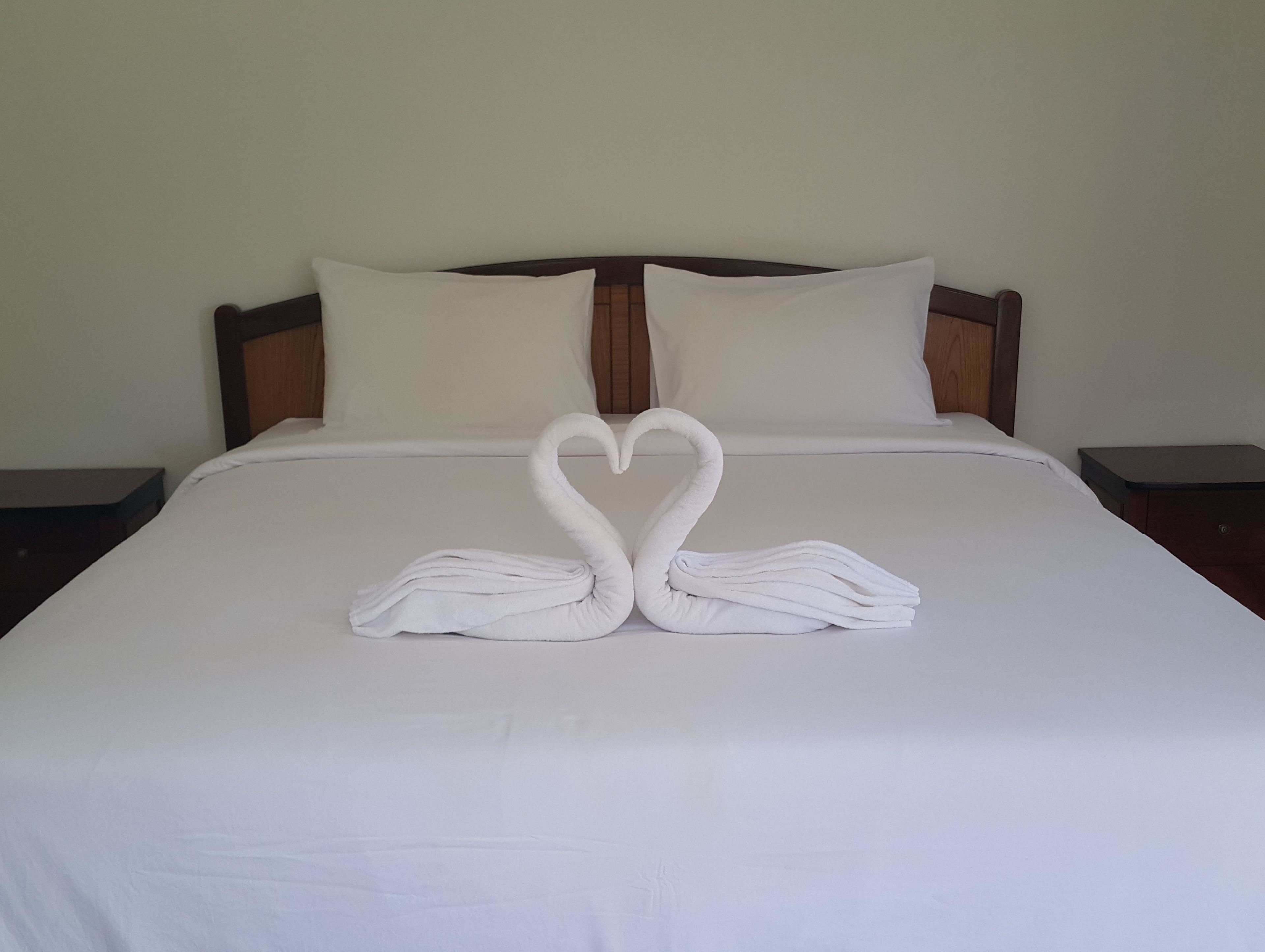A bed with white linens and two towels arranged in the shape of swans.
