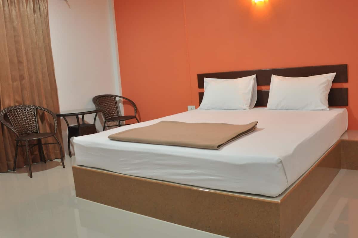 Una habitación de hotel con una cama, dos sillas, una mesa y una lámpara de pared.