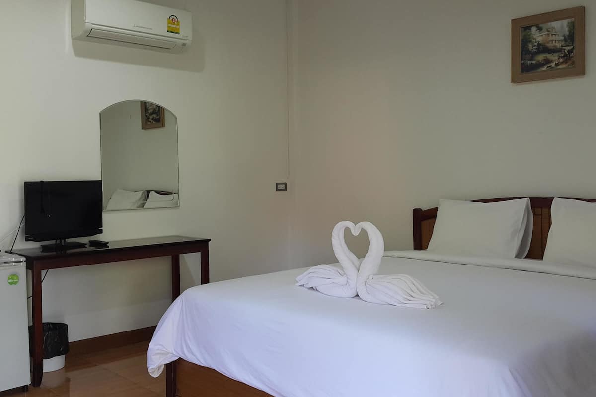 Una habitación de hotel con cama, escritorio, televisor, aire acondicionado y un cuadro en la pared.