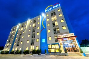 Un hotel de varios pisos con un llamativo letrero de 'Hop Inn', amplias ventanas y un área de entrada bien iluminada.