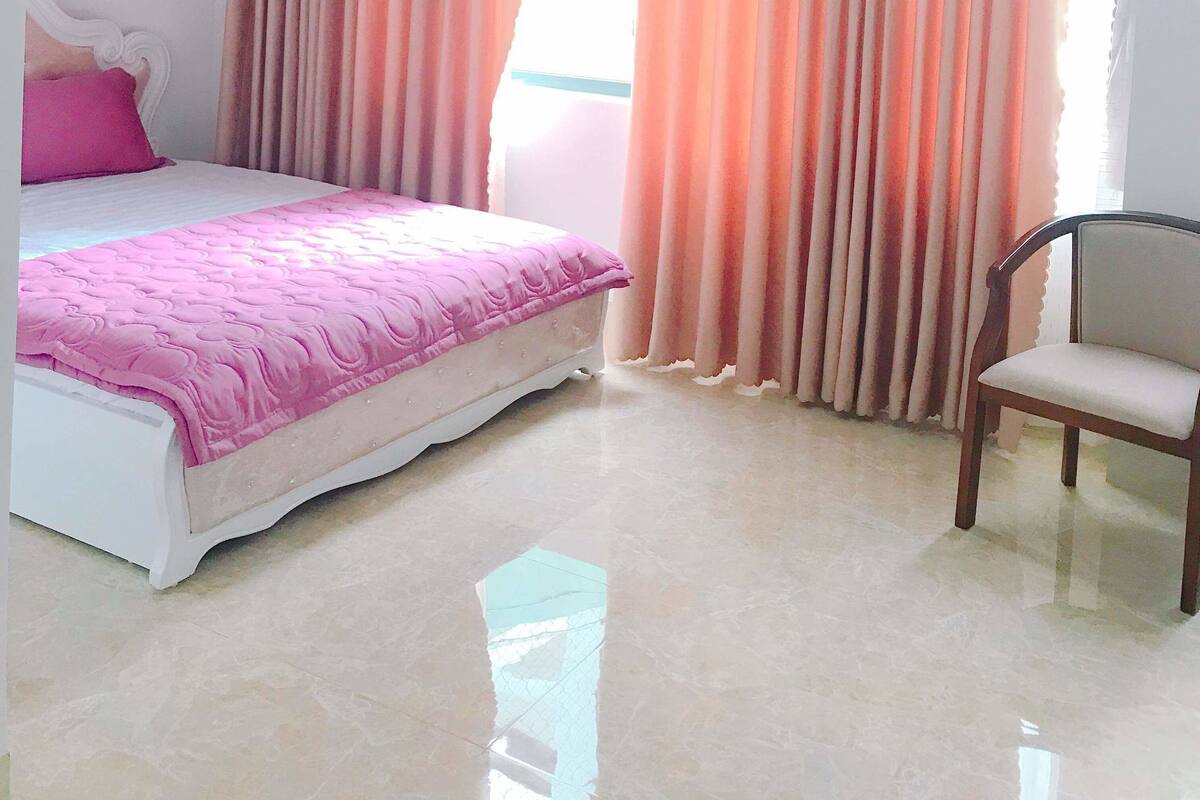 Un dormitorio con cama, una silla y cortinas.