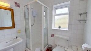Baño con ducha de vidrio, lavamanos, inodoro y ventana con una planta pequeña.
