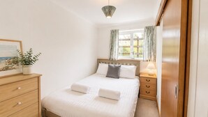 Un dormitorio ordenado con cama, mesita de noche, lámpara y ventana con cortinas.