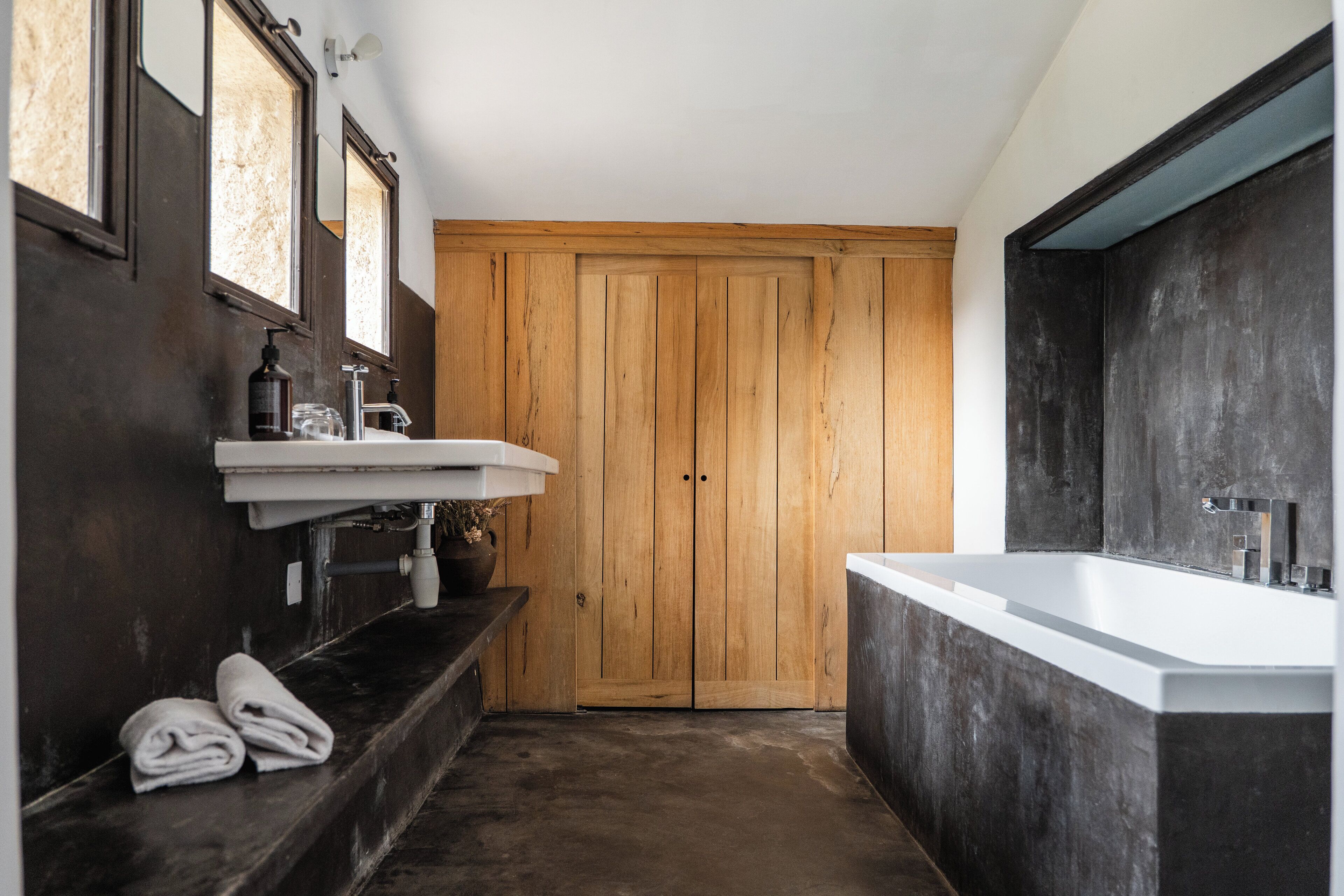 Un baño moderno con puerta de madera, un lavamanos blanco y una bañera grande.