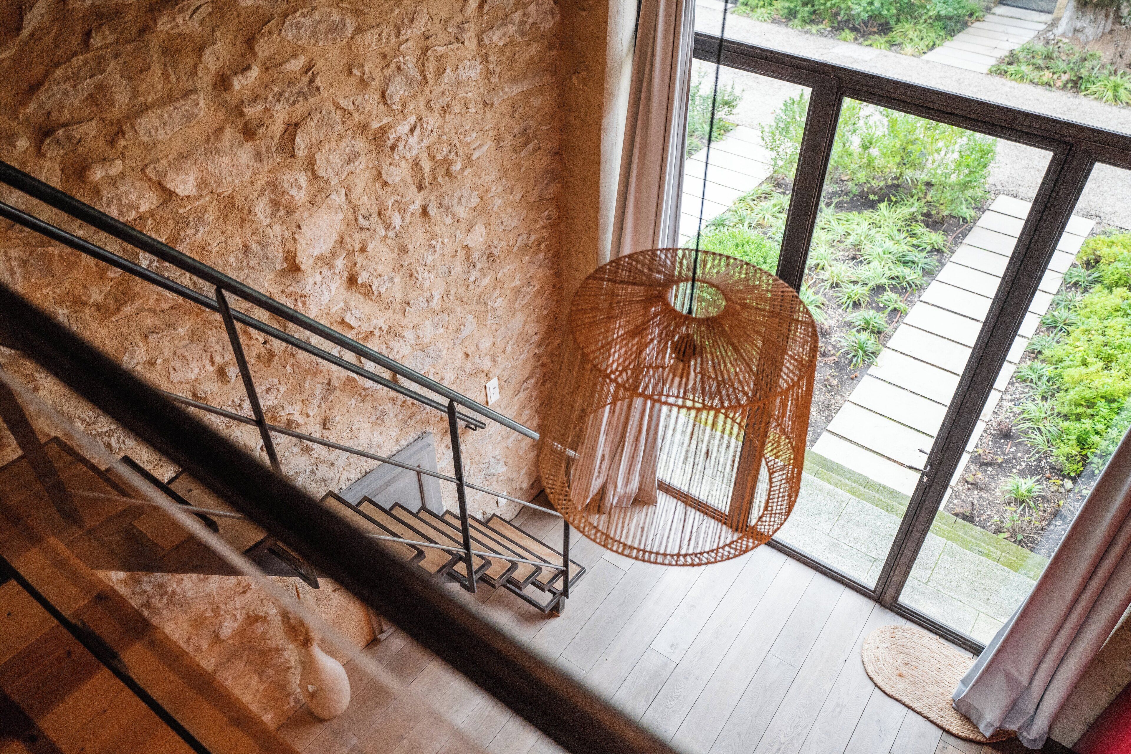 A staircase with a metal railing leading to a room with a large window and a wicker lamp.