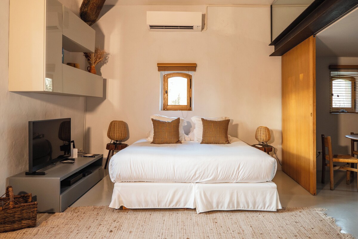 Un dormitorio con una cama grande, un televisor, una mesita y una ventana.