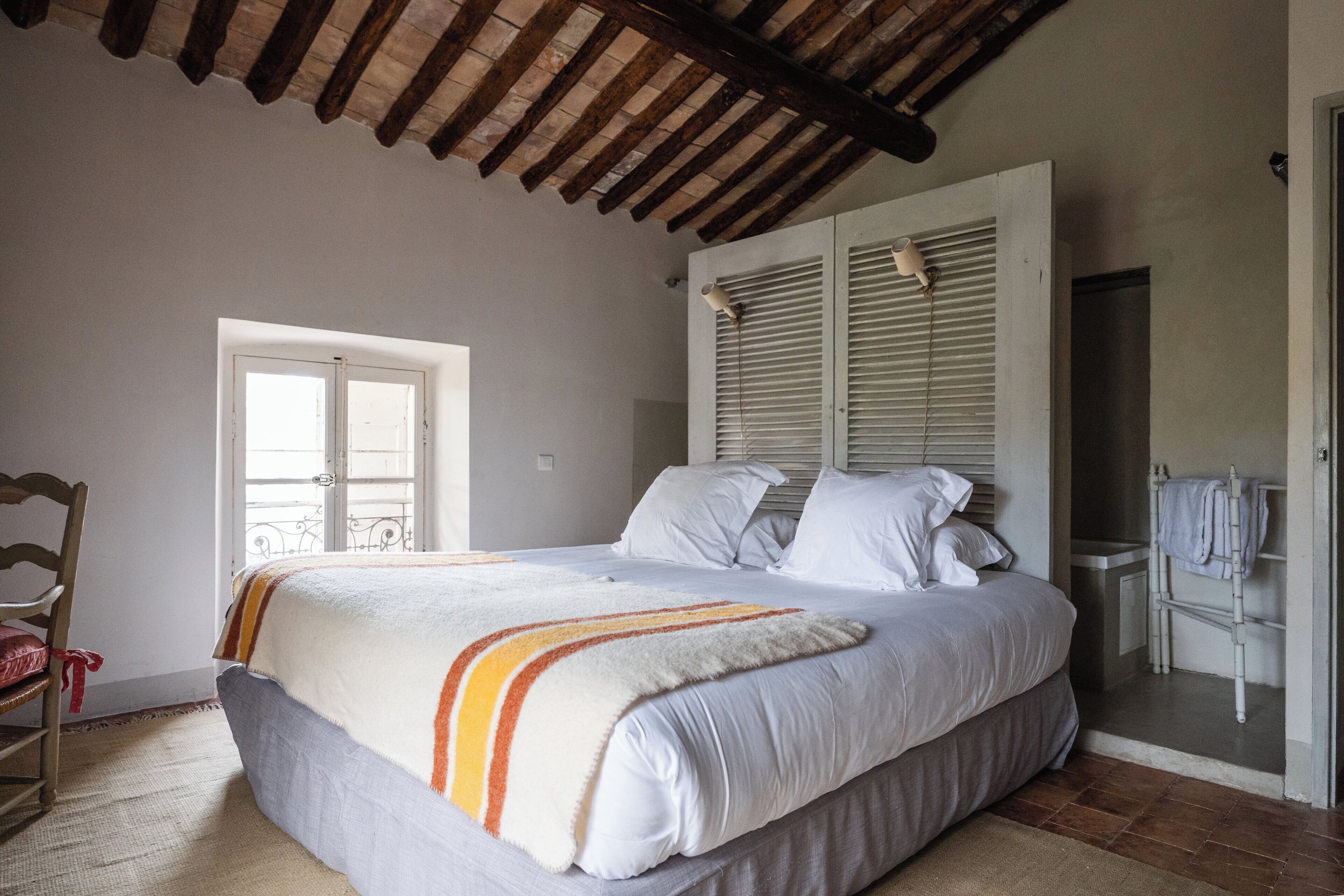 A bedroom with a bed, a wooden chair, a wardrobe, and a door leading to a balcony.