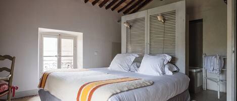 A bedroom with a bed, a wooden chair, a wardrobe, and a door leading to a balcony.