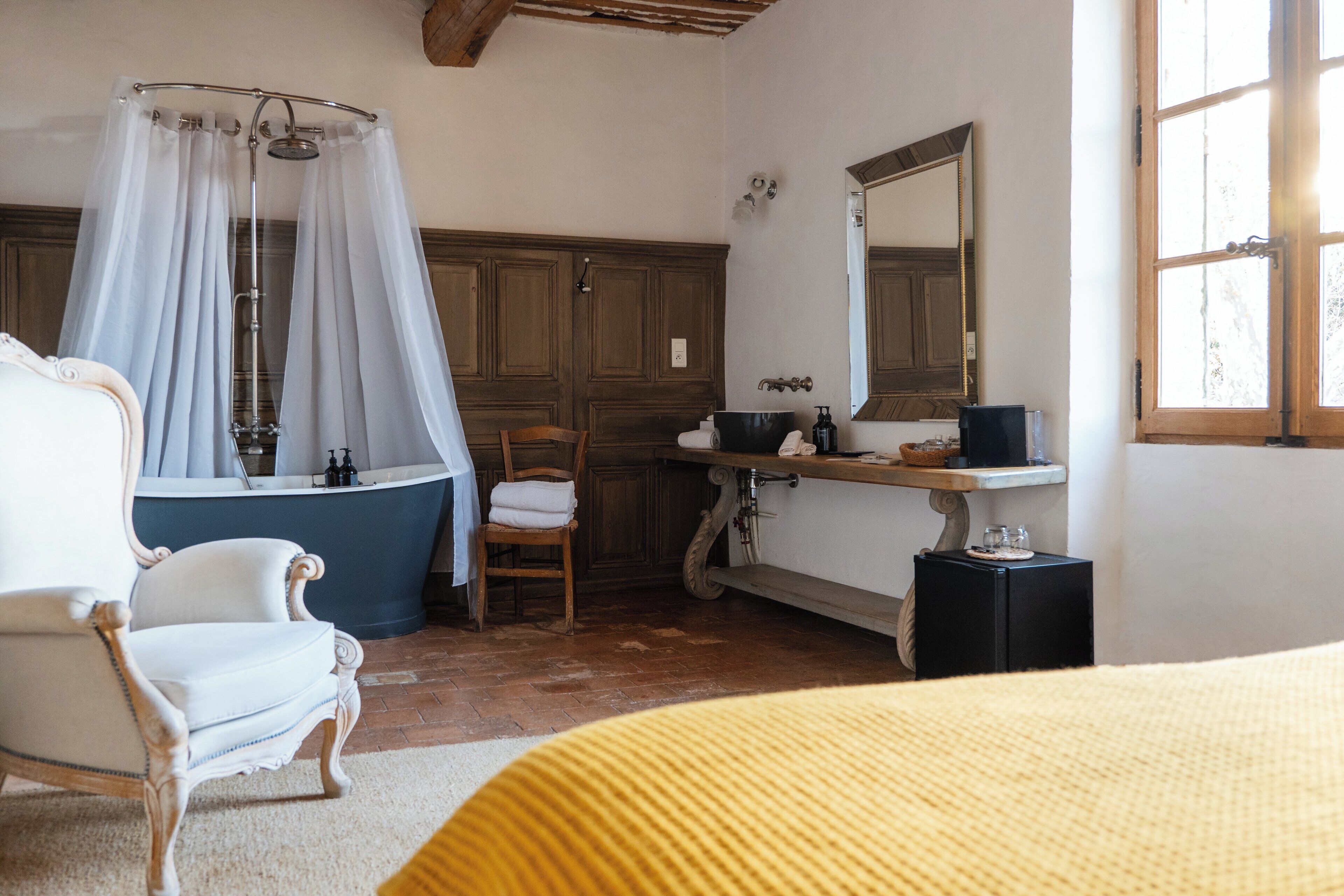 Un baño con bañera, una silla, un tocador con espejo y una ventana.
