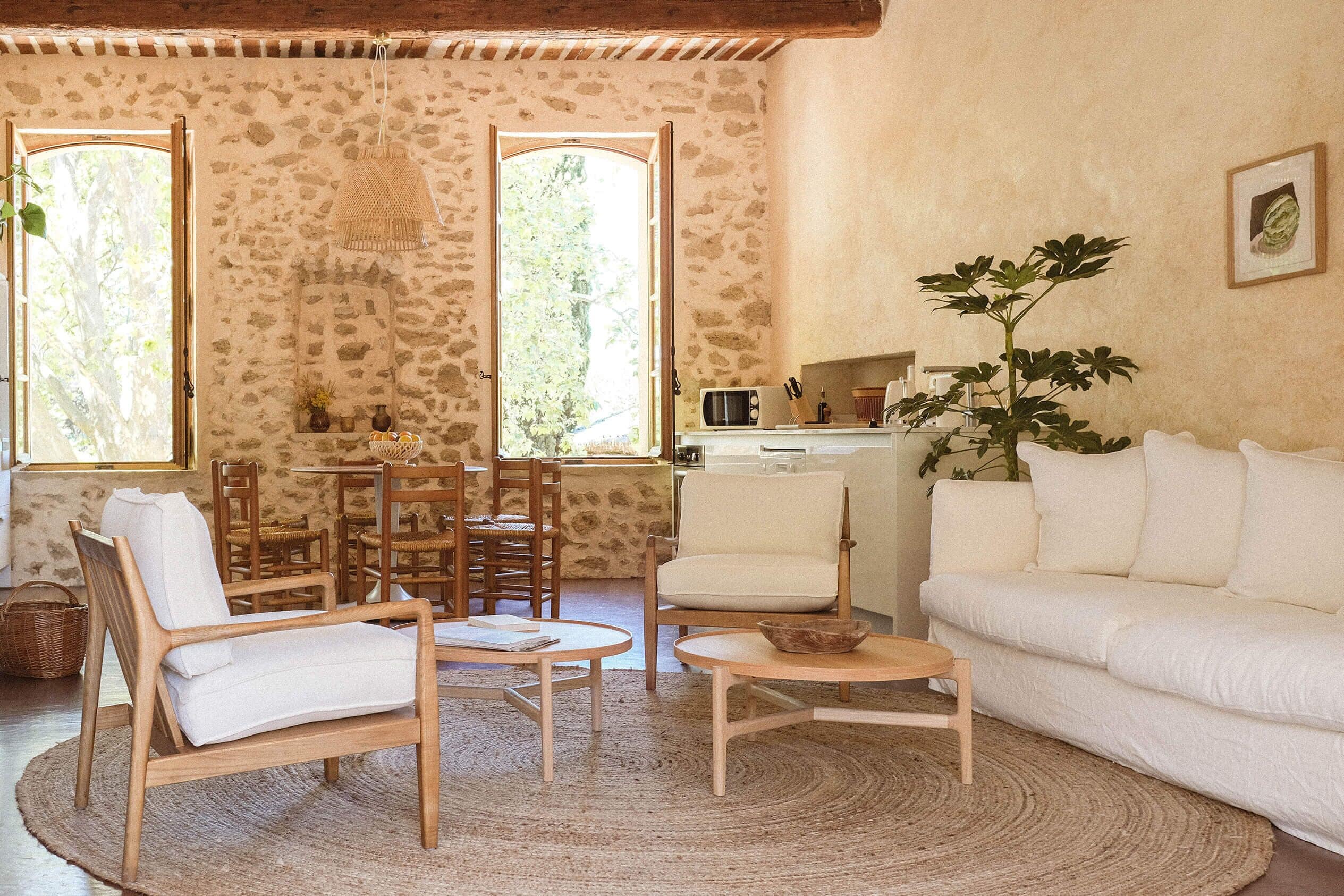A cozy living room with a stone wall, a white sofa, a wooden chair, a round coffee table, and a dining area with a table and chairs.