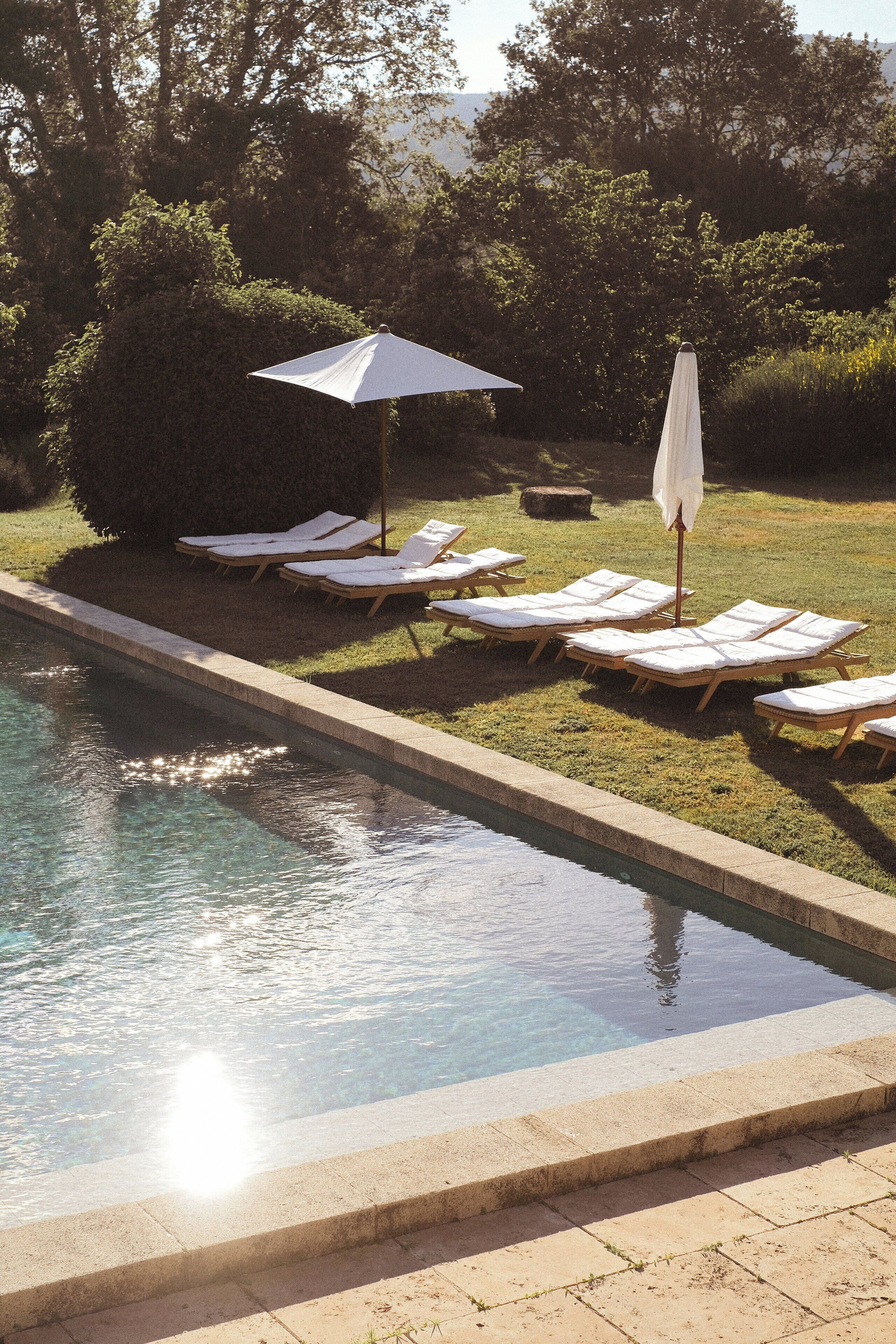Piscina com espreguiçadeiras e guarda-sóis, rodeada por vegetação.