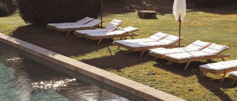 Piscina com espreguiçadeiras e guarda-sóis, rodeada por vegetação.