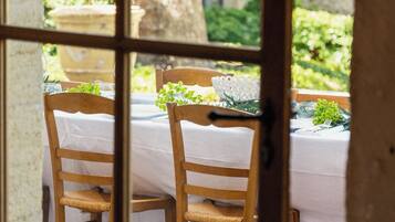 A rustic dining area with a table set for two, wooden chairs, and a view of greenery outside.