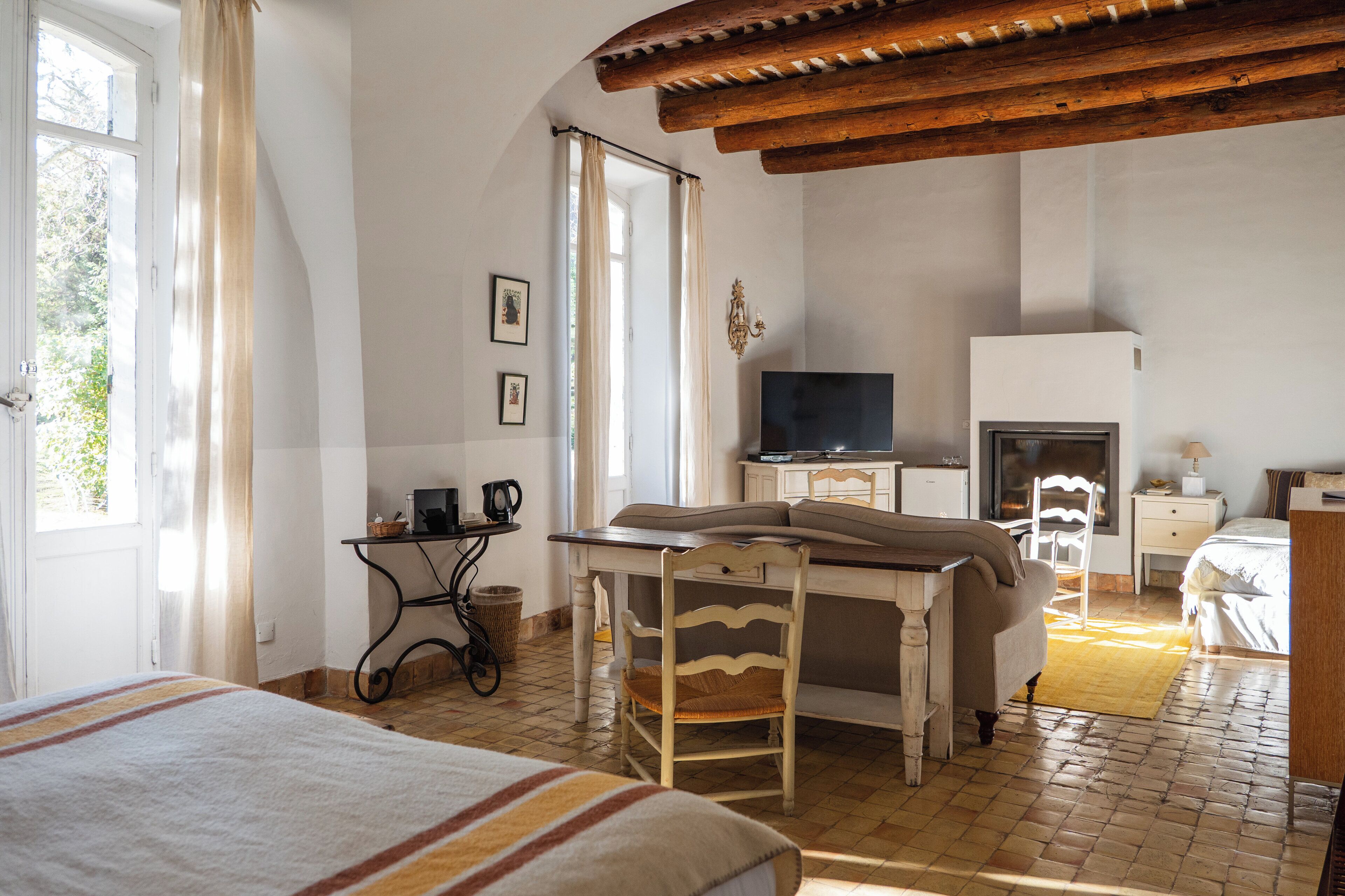A bedroom with a bed, a desk, a chair, a television, and a fireplace.
