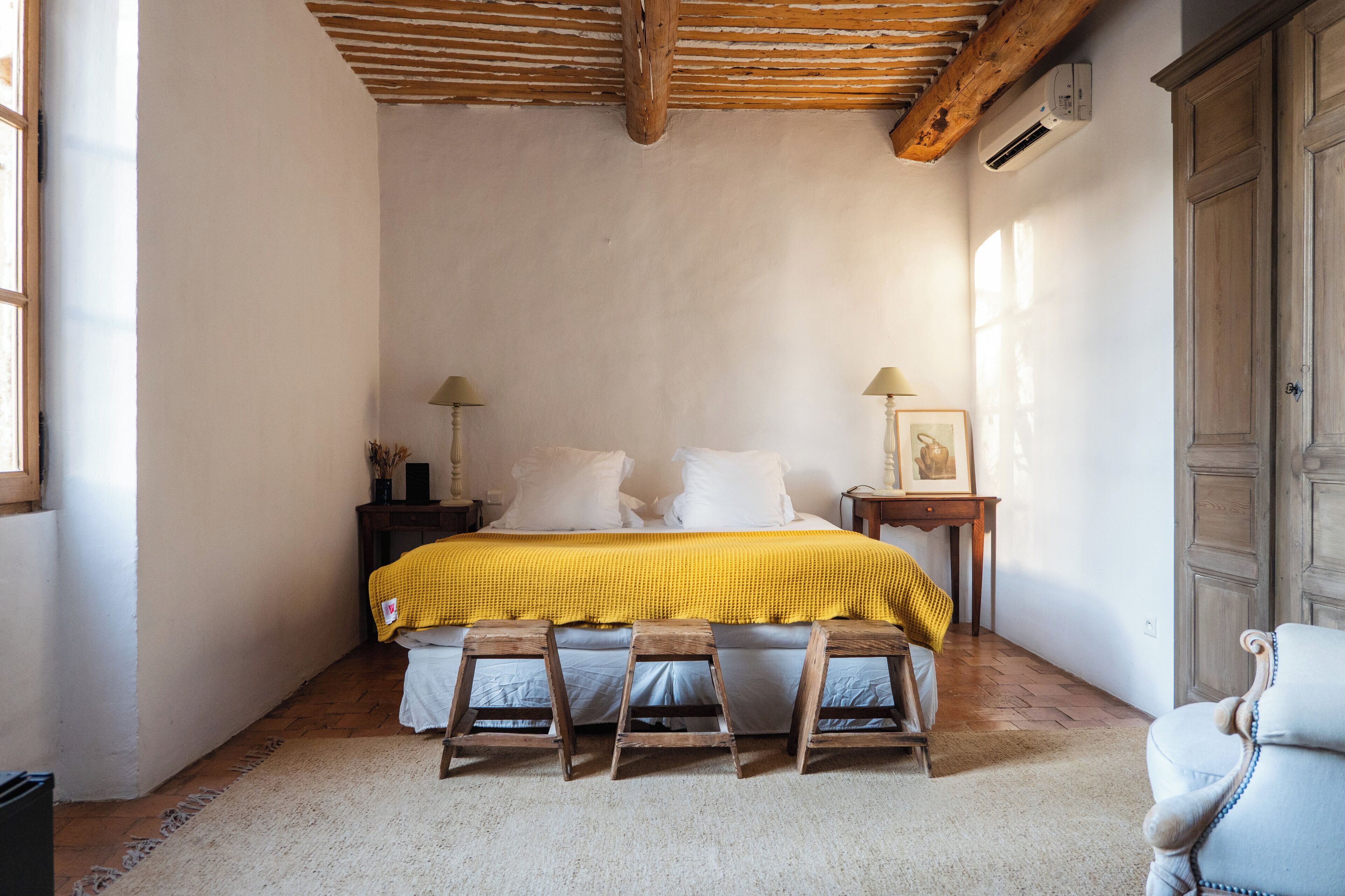 A bedroom with a bed, wooden stools, a chair, a nightstand, and a wardrobe.
