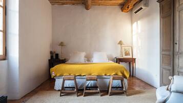 A bedroom with a bed, wooden stools, a chair, a nightstand, and a wardrobe.