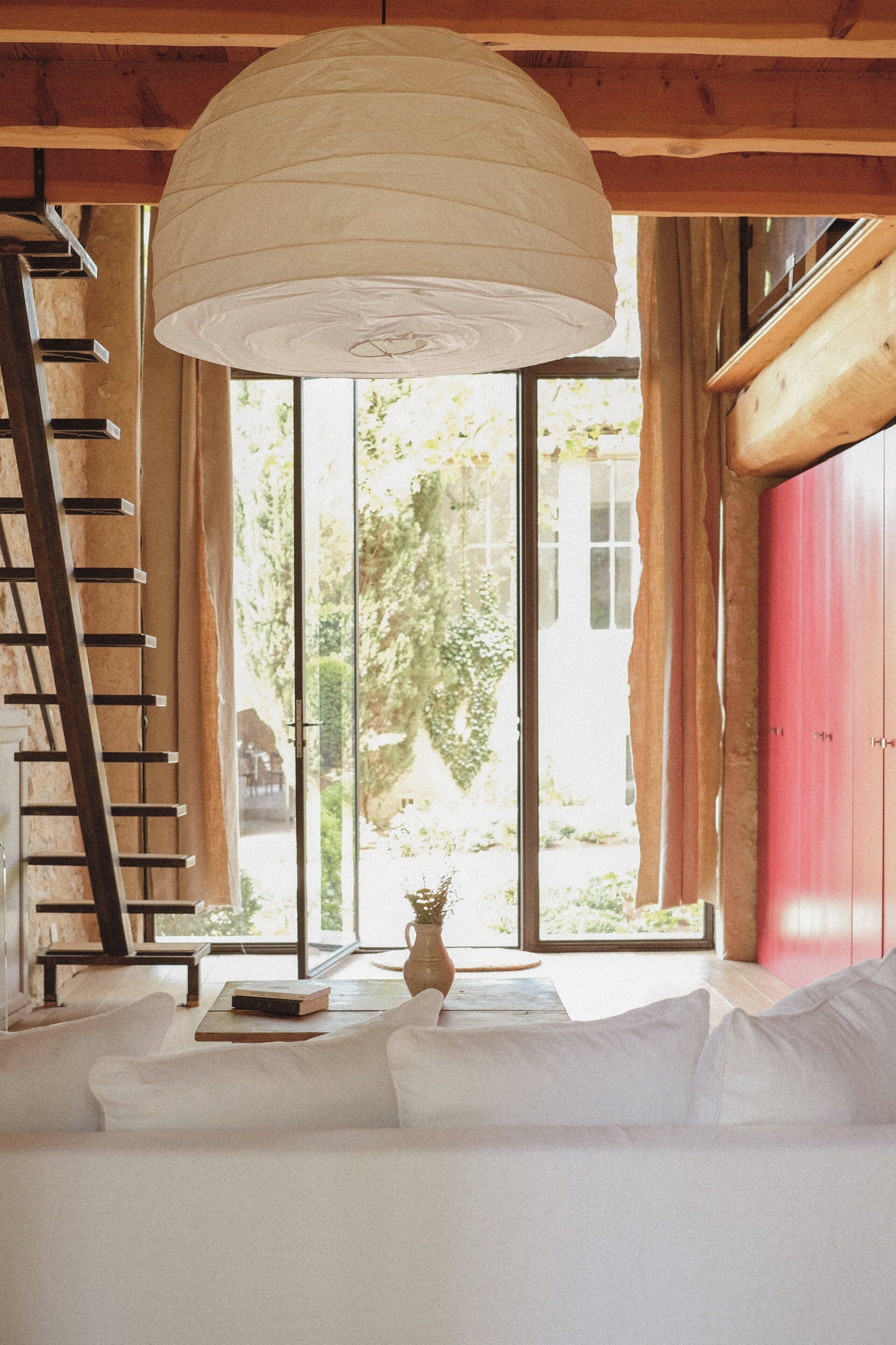 A room with a wooden ceiling, a white sofa, a ladder, and a large window with curtains.