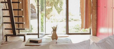 A room with a wooden ceiling, a white sofa, a ladder, and a large window with curtains.