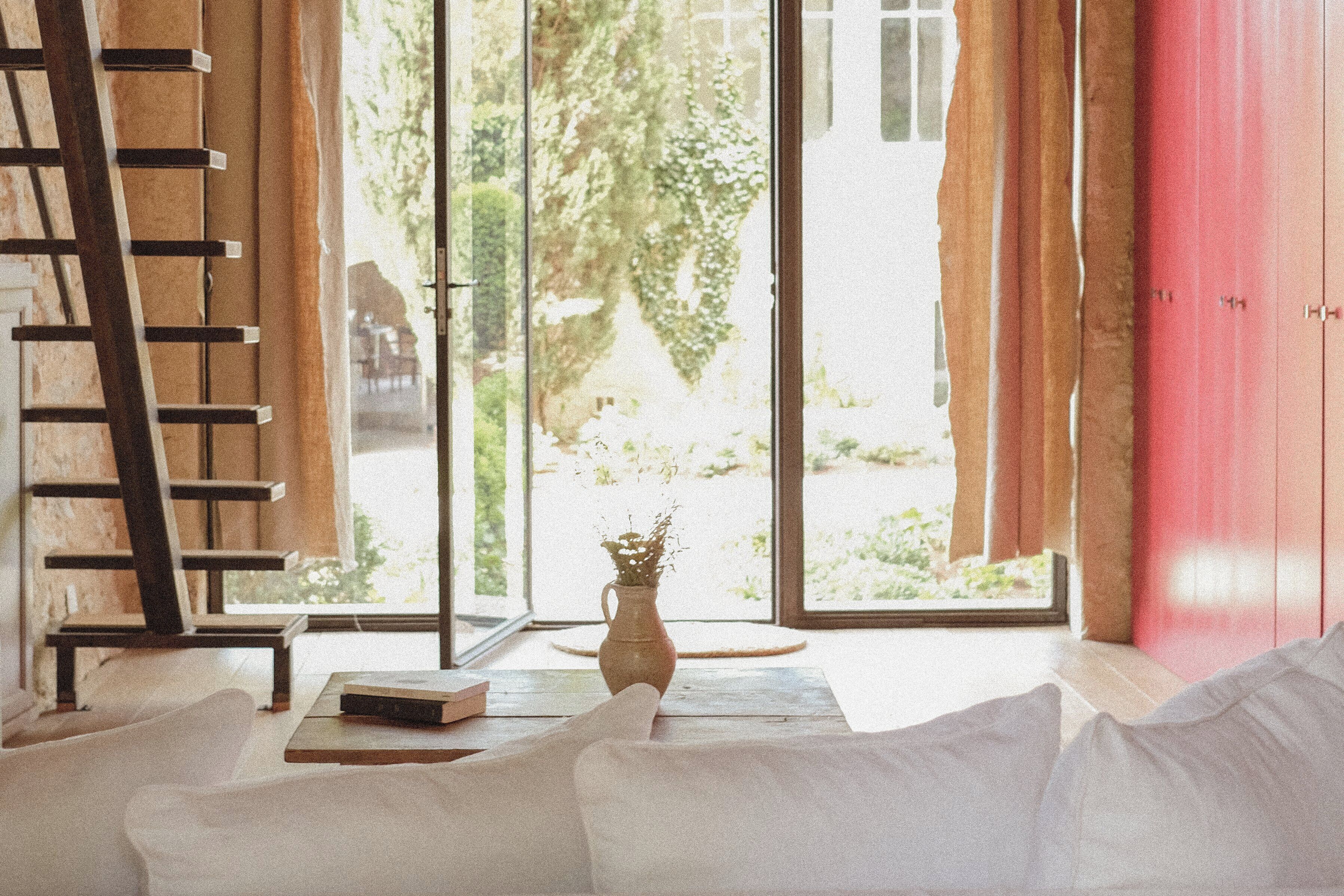 Ein Zimmer mit einer Holzleiter, einer Blumenvase und einem Buch auf einem Tisch.