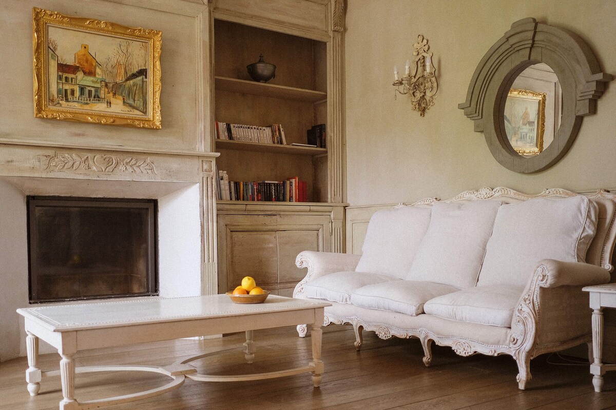 Una habitación con chimenea, un sofá blanco, una mesa con frutero y una estantería.