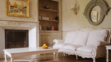 Una habitación con chimenea, un sofá blanco, una mesa con frutero y una estantería.