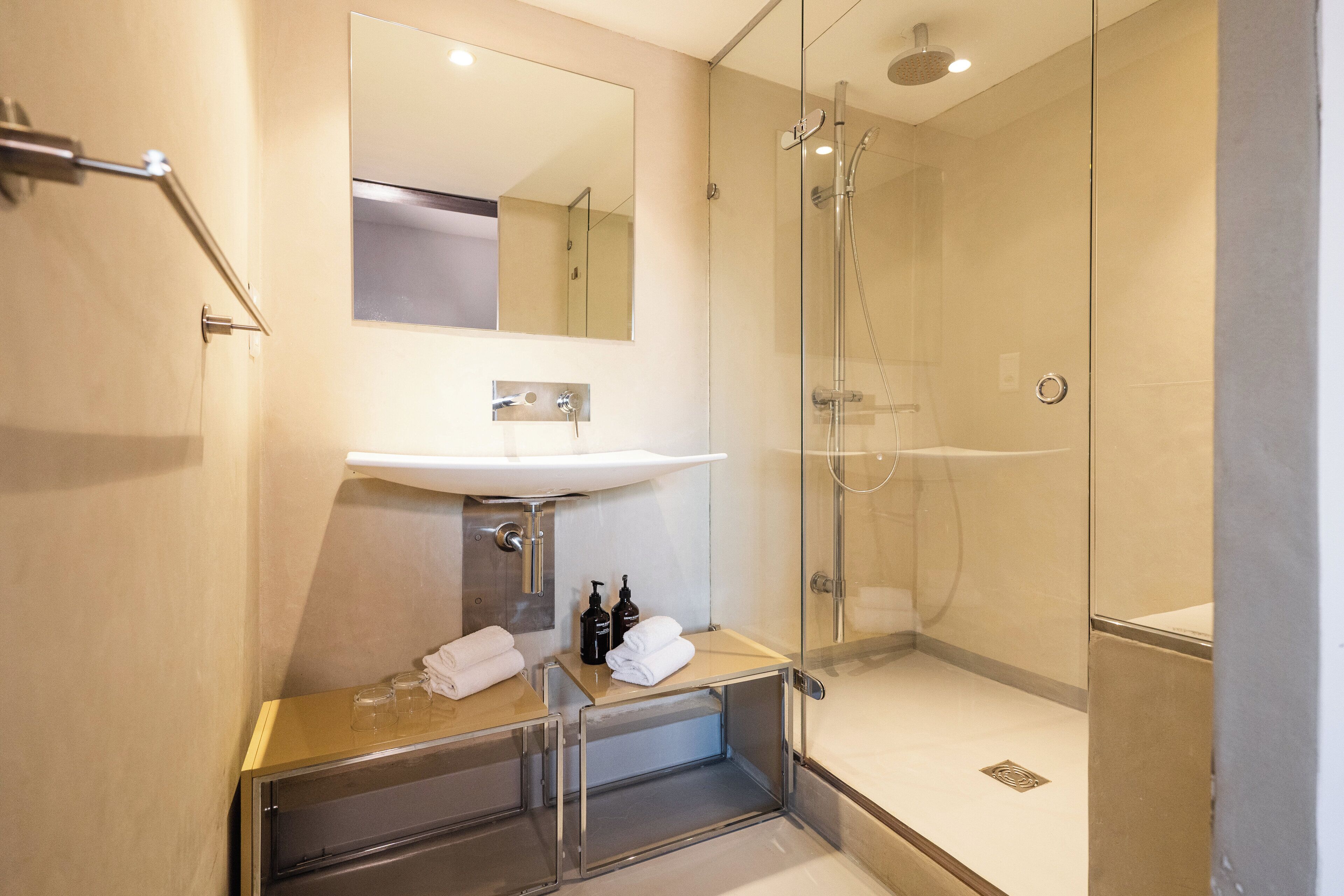Une salle de bain moderne avec une douche à parois de verre, un lavabo avec un miroir au-dessus et une petite étagère contenant des articles de toilette.
