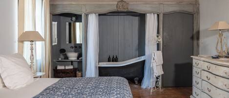 A bedroom with a large bed, a vanity with a mirror, a bathtub, and a wooden ceiling.
