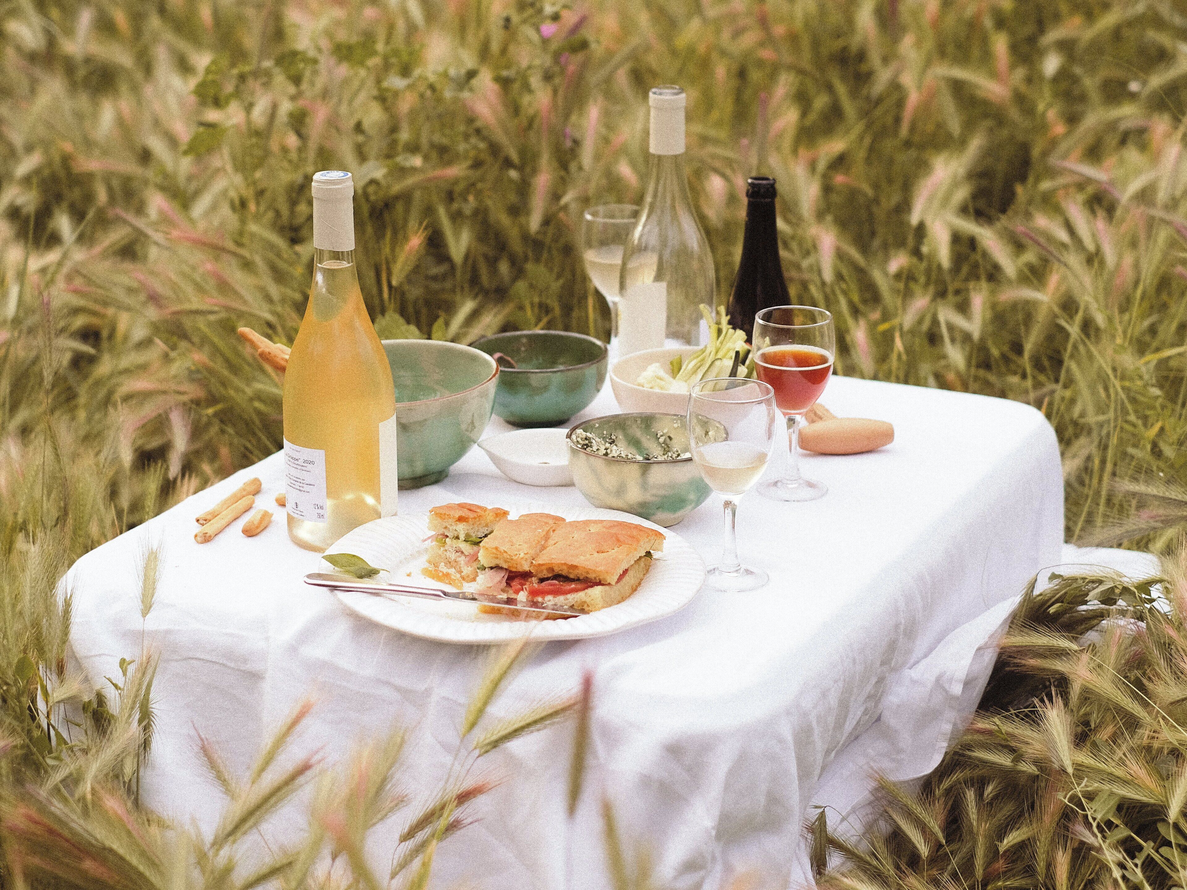 Ein Picknick mit weißem Tuch, Essen und Getränken auf einer Wiese.