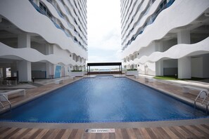 Een modern zwembadgedeelte van een hotel, met een centraal gelegen zwembad, omgeven door witte balkons en een overdekt zitgedeelte.