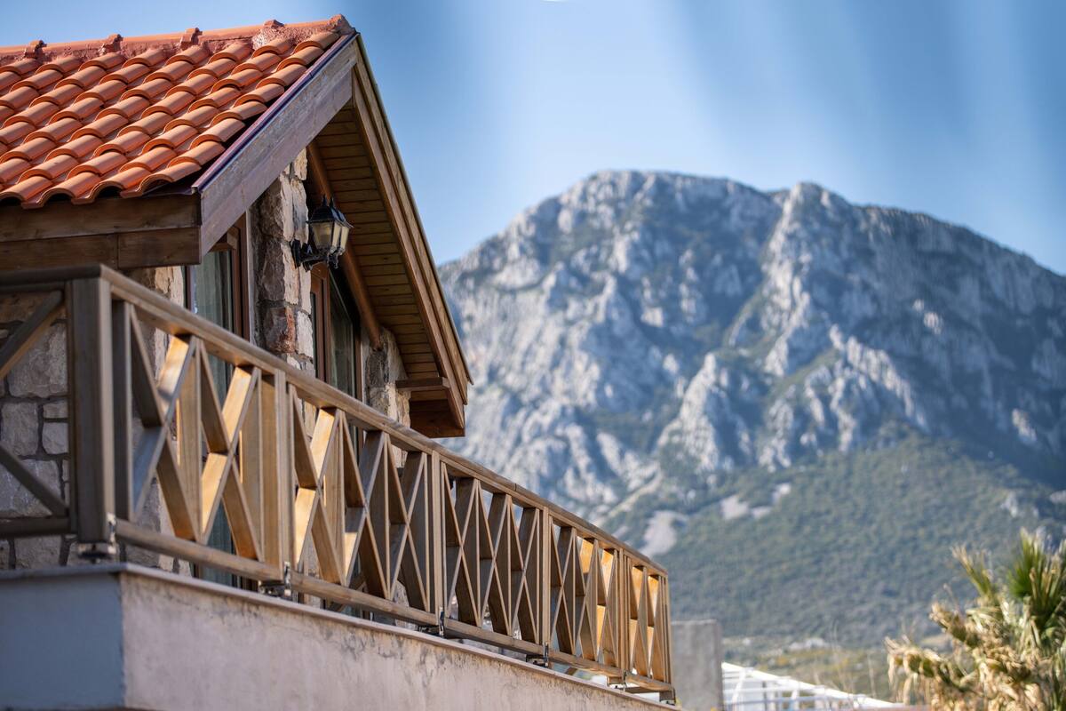 A building with a tiled roof and a balcony with a wooden railing. In the background, there is a mountain.
