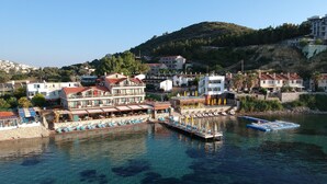 A waterfront hotel with multiple balconies, a pool area, and clear blue water. - Tasada Otel (Karaburun)