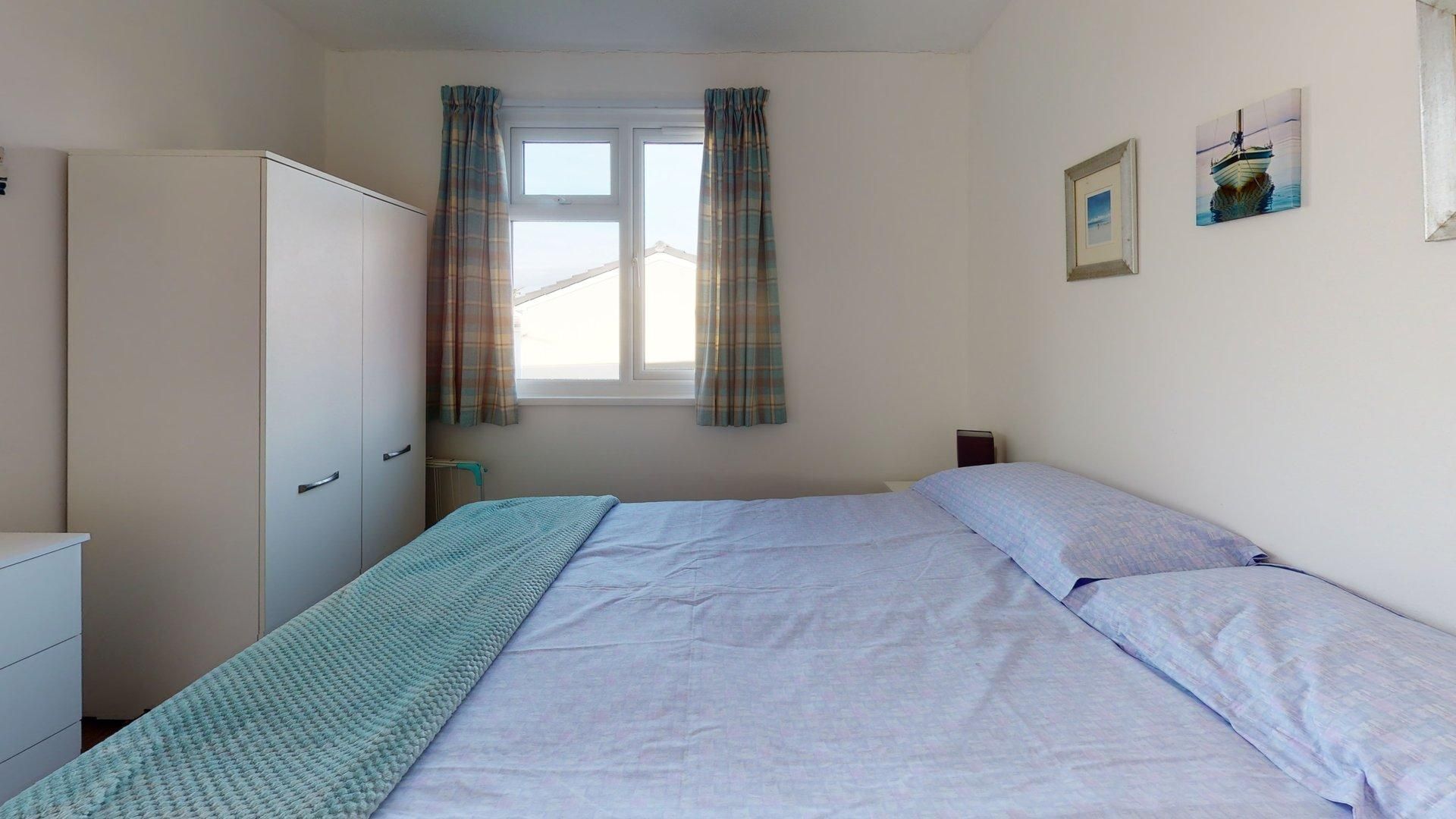 Ein Schlafzimmer mit einem Bett, einem Kleiderschrank, einem Fenster mit Vorhängen und zwei Bildern an der Wand.