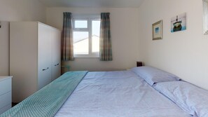 Quarto com cama, guarda-roupa, janela com cortinas e duas imagens penduradas na parede.