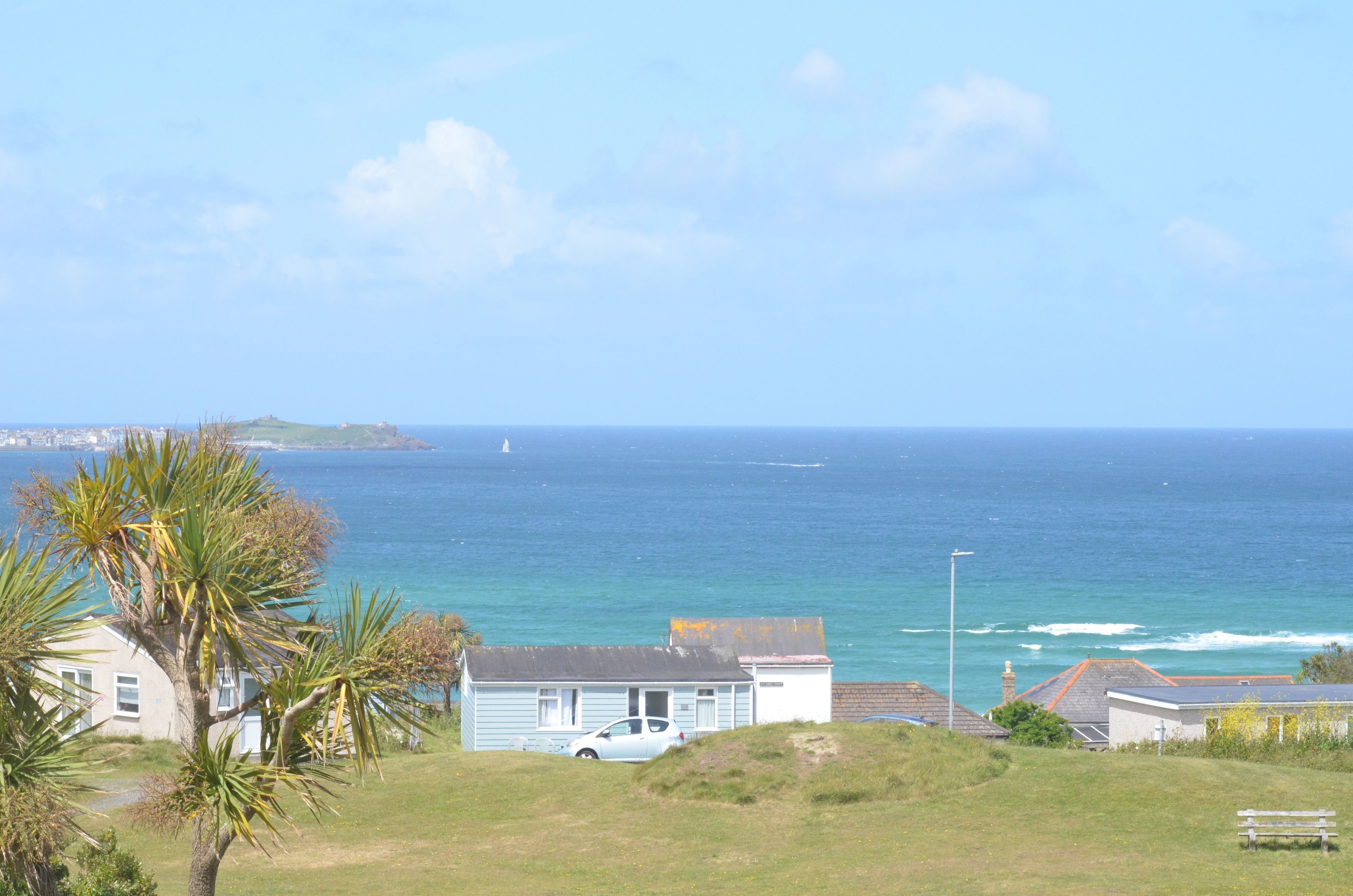 A coastal view with a house, a parked car, and a palm tree.