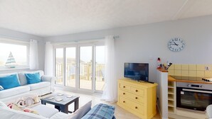 Een lichte woonkamer met een witte bank, een televisie en een geel kastje.