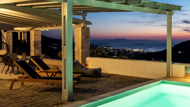 Area piscina esterna con lettini e una pergola, affacciata su un panorama urbano al crepuscolo.