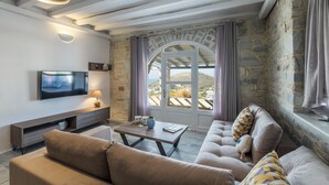 Un soggiorno moderno con parete in pietra, un'ampia finestra ad arco, una TV a schermo piatto e un divano con cuscini decorati.