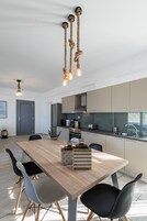 A modern kitchen with a wooden dining table, chairs, and a hanging light fixture.